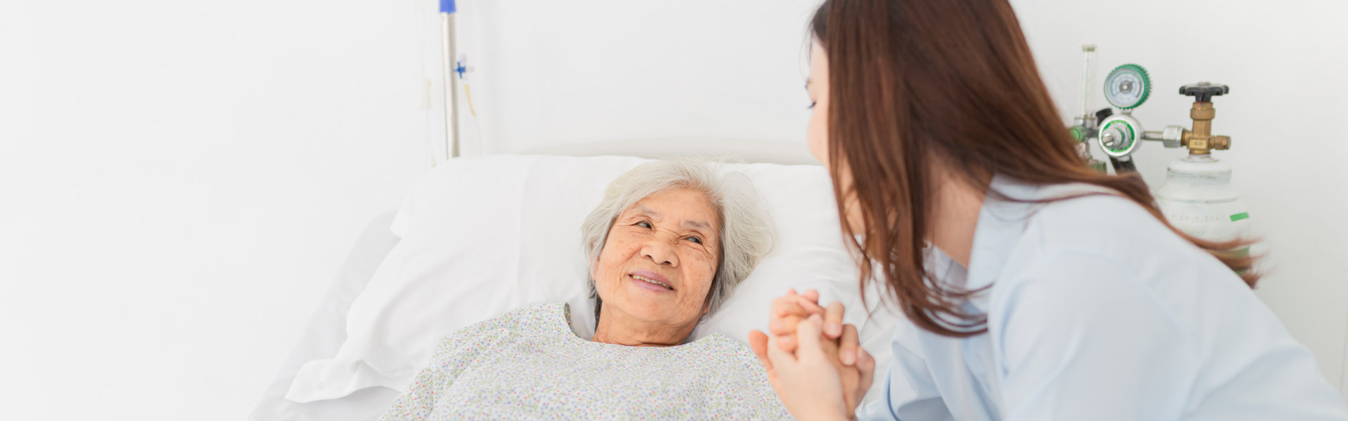 caregiver holding the hands of the elderly in bed